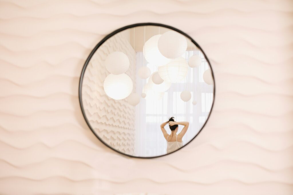 Round mirror on a blush wall showing a woman