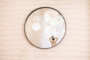 Round mirror on a blush wall showing a woman